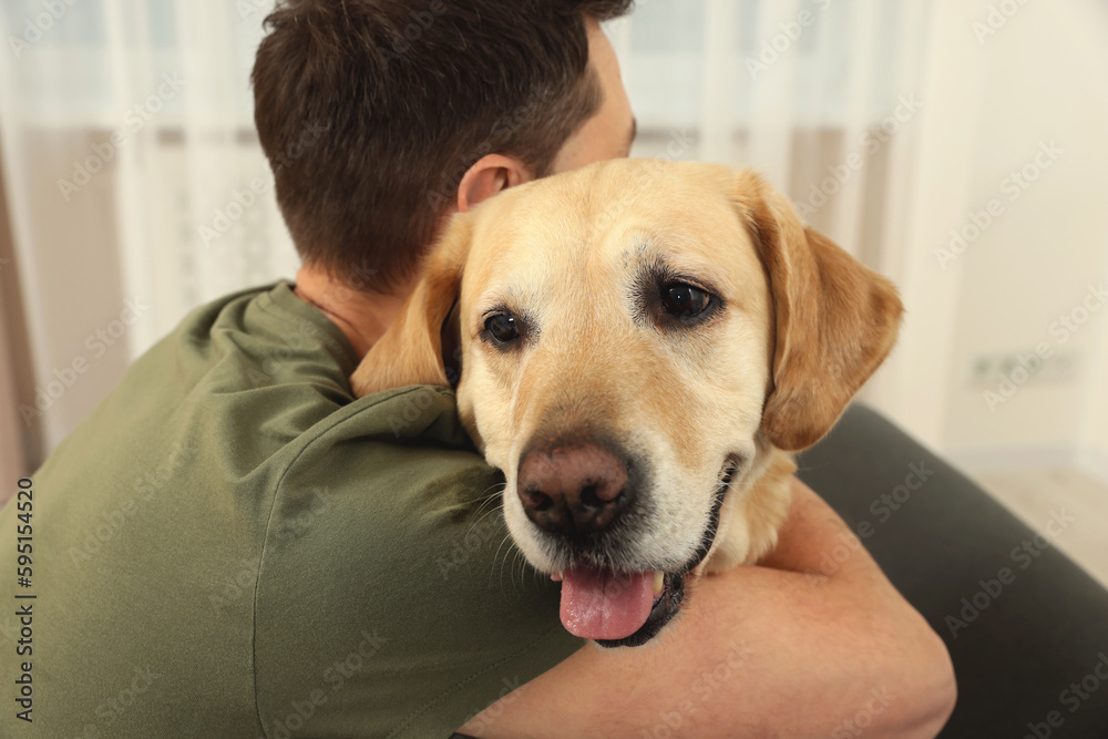Man hugging his cute Labrador Retriever at home, back view
