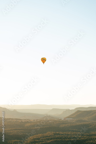 Vertical image of wide shot of hot air balloon isolated against white sky background in early morning flight.
