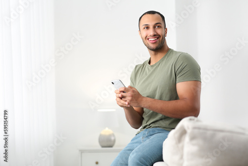Smiling African American man with smartphone on sofa at home. Space for text