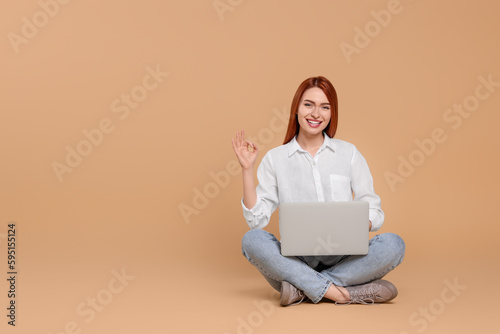 Smiling young woman with laptop showing OK gesture on beige background, space for text