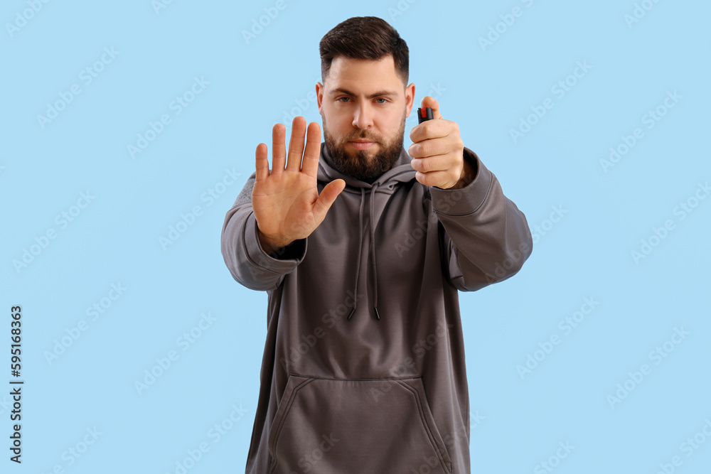Fototapeta premium Young man with pepper spray for self-defence on blue background