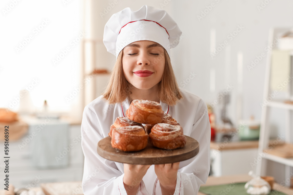 Female baker with board of tasty buns in kitchen, closeup Female baker with board of tasty buns in kitchen, closeup