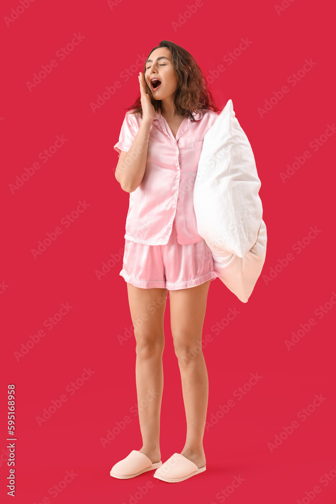 Young brunette woman in pajamas with pillow on pink background Young brunette woman in pajamas with pillow on pink background