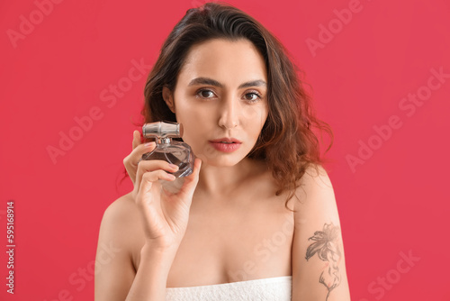 Young brunette woman with bottle of perfume on pink background, closeup