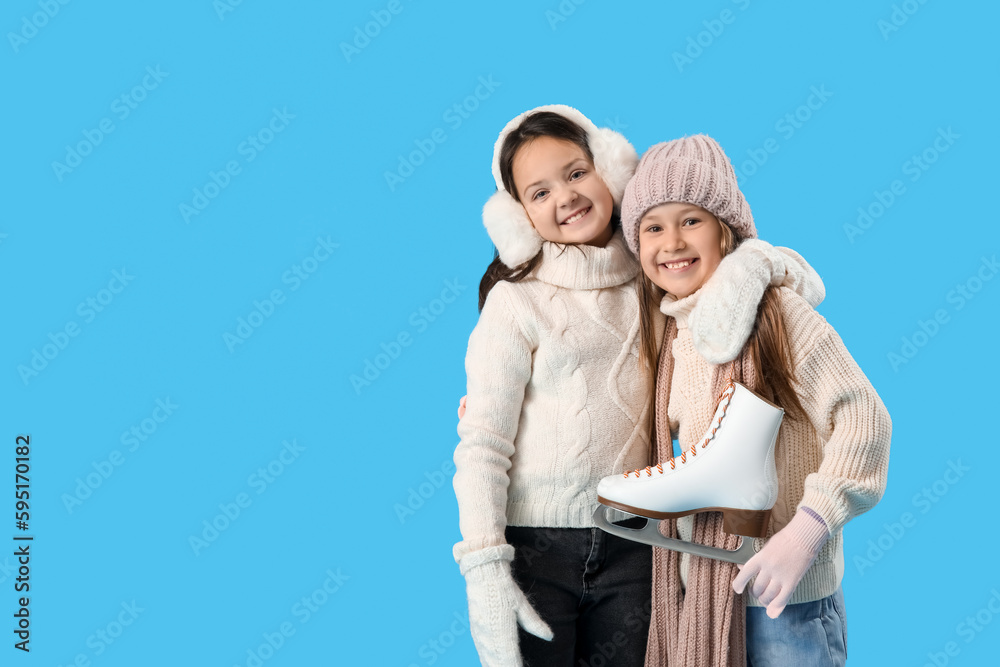 Little girls in winter clothes with ice skates hugging on blue background Little girls in winter clothes with ice skates hugging on blue background