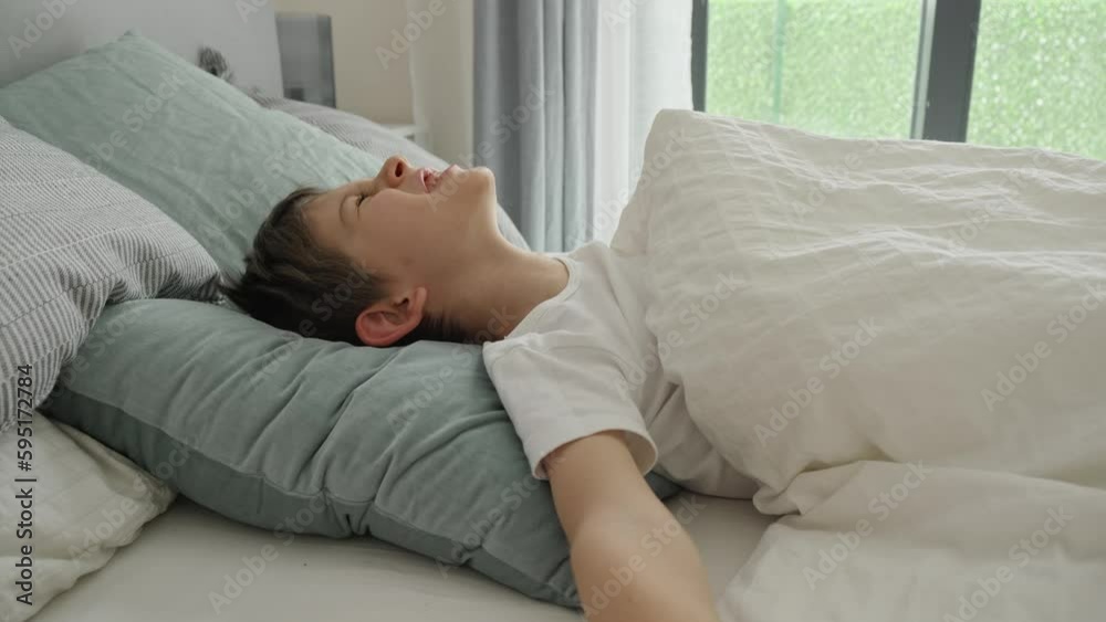 Portrait of smiling boy waking up in bed at morning, yawning and stretching out hands