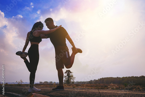 Silhouette of young couple warming up  stretching their muscle at the road track outdoor with sunset background. Fit runner workout and warming up