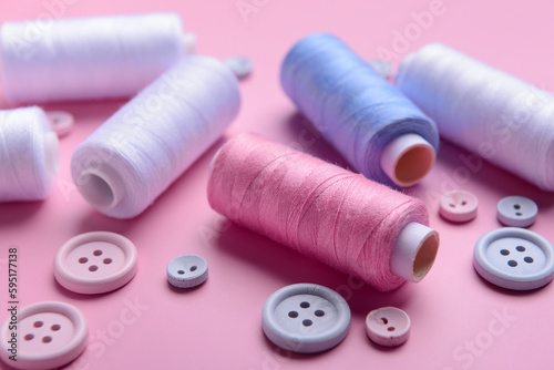 Different thread spools and buttons on pink background, closeup