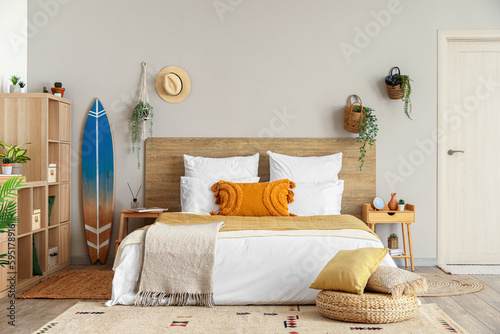 Interior of light bedroom with surfboard, houseplants and shelving unit