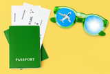 Green passport, boarding pass, flight ticket, sunglasses, flying airplane, sun blue sky, summer holiday, vacation concept, travel banner, international airlines, tourism, yellow background, copy space
