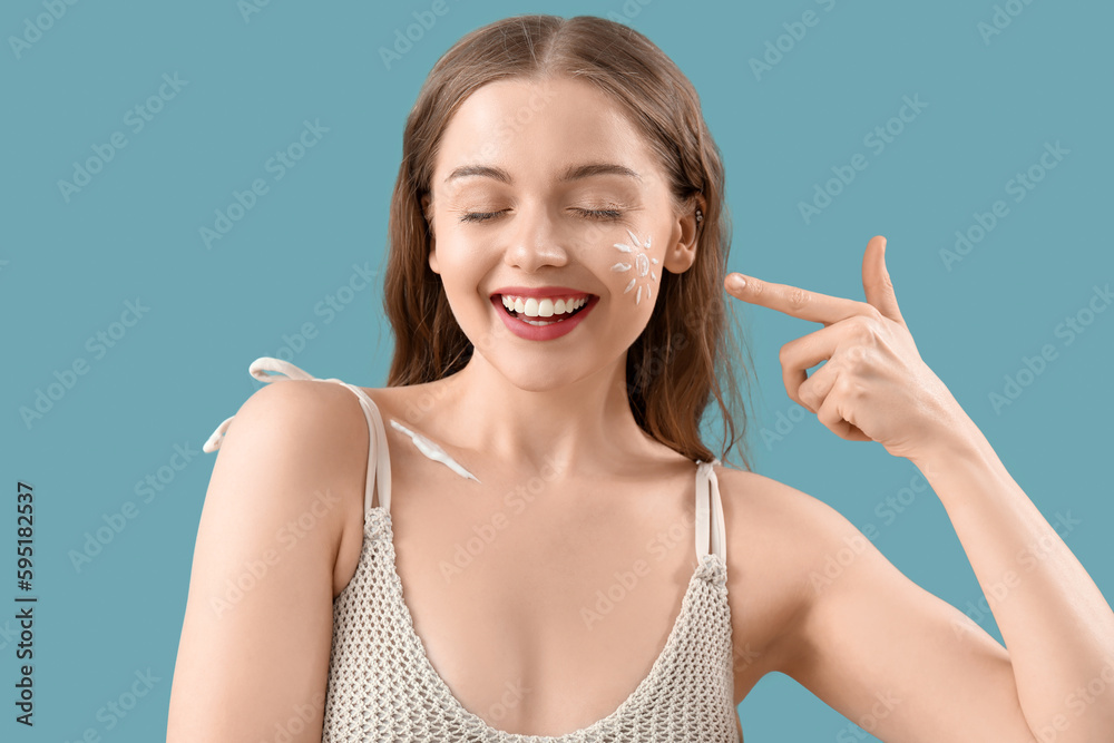 Beautiful young woman with sunscreen cream on her face against blue background