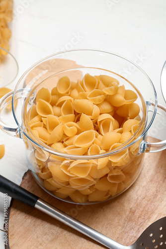 Pot with raw conchiglie pasta on light wooden background photo