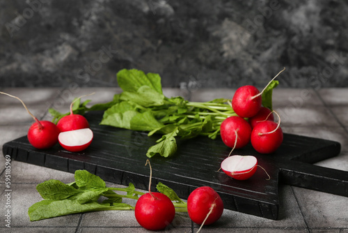 Wooden board of ripe radish with green leaves on table