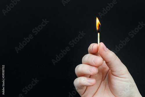 Hands holding burning match on black background. Copy space.