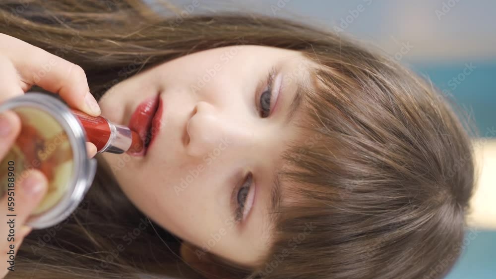 Vertical Video of Little girl paints her lips with lipstick. Doing makeup. Vertical Video of Little girl paints her lips with lipstick. Doing makeup.