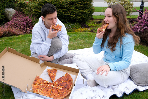 boy and girl teenagers eat pizza sitting on a blanket in nature sportswear adolescence communication friends first date delicious food fast food pizza delivery takeaway park