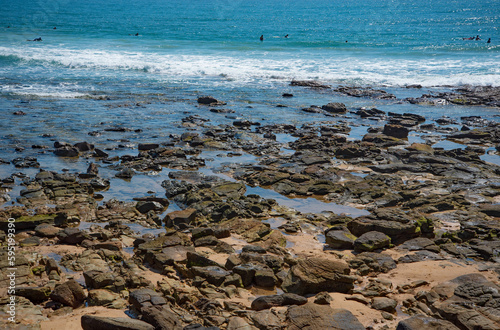 Surfers paddling out at Alexandra Headlands with rocks.