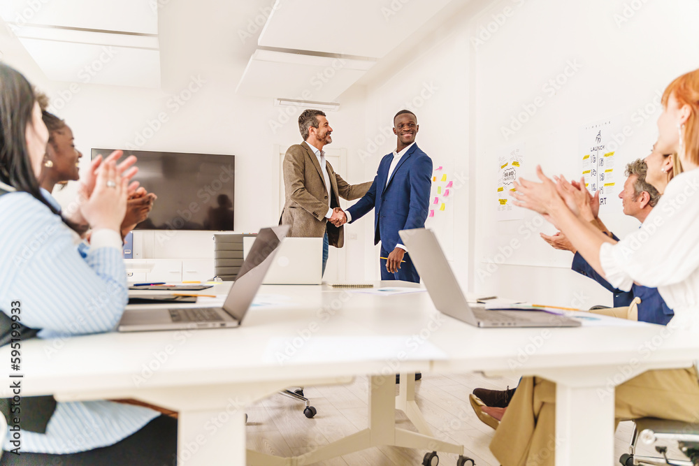 Obraz premium Office Handshake Celebration - Wide shot of a diverse office, two people shaking hands in the center, colleagues applauding. Signifies collaboration or success.