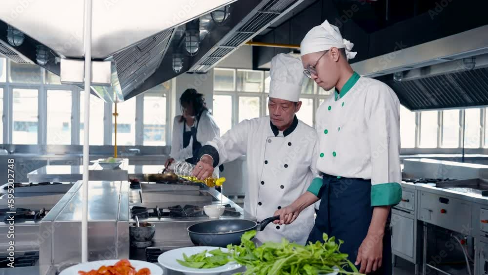 4K Slow, Assistant chef, chef are helping each other prepare food in kitchen, chef hands bottleoil poured into pan assistant prepare food, In background are two female students standing and talking. 4K Slow, Assistant chef, chef are helping each other prepare food in kitchen, chef hands bottleoil poured into pan assistant prepare food, In background are two female students standing and talking.