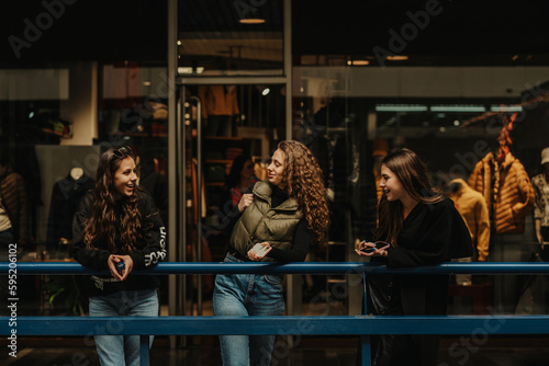 Three girls talking fashion while leaning on a blue fence at the shopping mall
