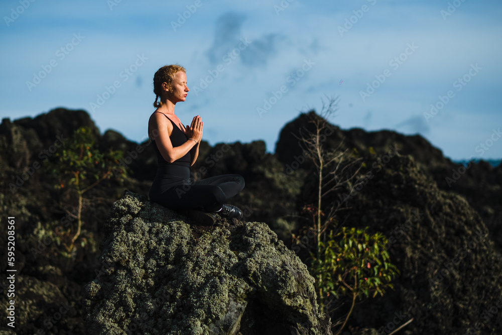 A young beautiful girl, a yogini, sits in the mountains, with her eyes closed, clasped her hands in namaste and meditates. A young beautiful girl, a yogini, sits in the mountains, with her eyes closed, clasped her hands in namaste and meditates.