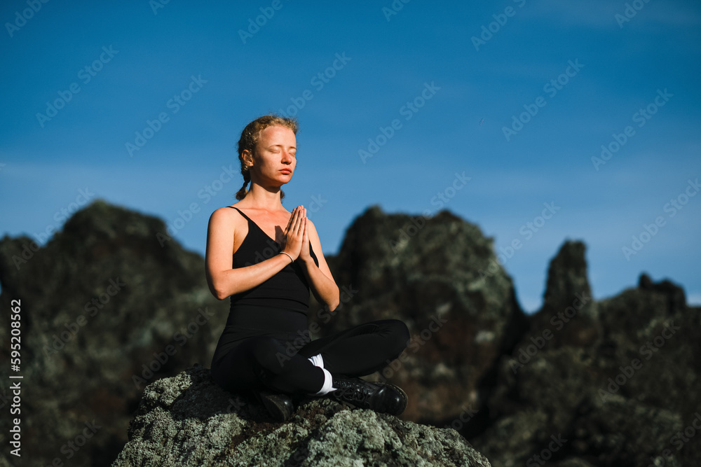 A young beautiful girl, a yogini, sits in the mountains, with her eyes closed, clasped her hands in namaste and meditates. A young beautiful girl, a yogini, sits in the mountains, with her eyes closed, clasped her hands in namaste and meditates.