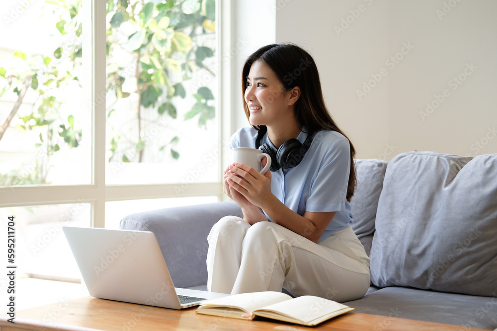 Coffee, laptop and Asian woman on couch, headphones and relax in home, calm and watching video. Japan, female and happy lady with headset, device and tea in living room, happiness and social media Coffee, laptop and Asian woman on couch, headphones and relax in home, calm and watching video. Japan, female and happy lady with headset, device and tea in living room, happiness and social media