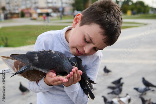 Close-up portrait of a schoolboy feeding rock pigeons in the park. The concept of kindness, walking with benefits, love and care for animals. Installing compassion for animals from childhood