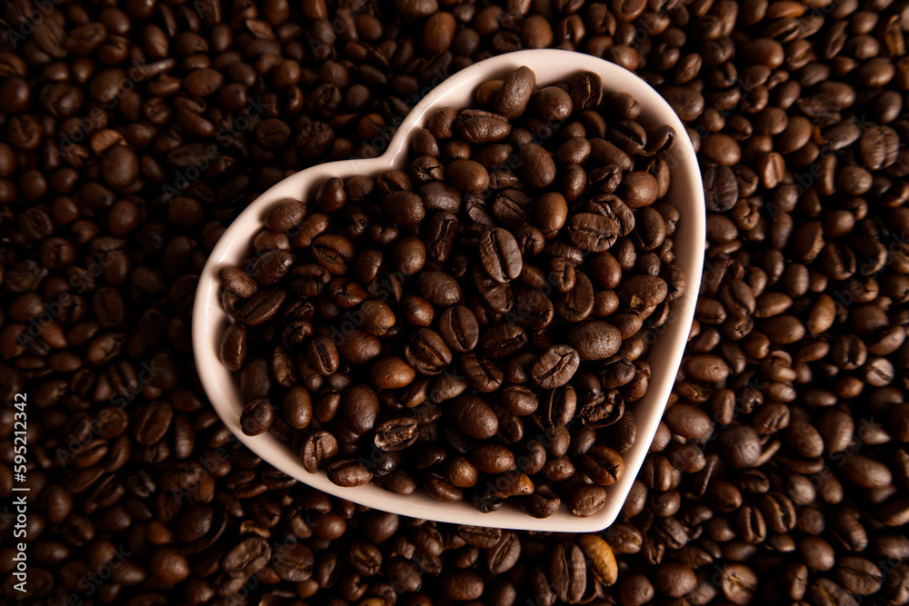Close-up roasted coffee beans in a heart-shaped plate on a coffee background
