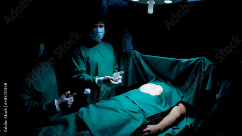 Man lying in operating room, doctors are installing surgical instruments, attached chest on patient's torso long tubular instrument, female doctor checks whether installed cable is secure enough.