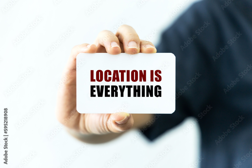 Location is everything text on blank business card being held by a woman's hand with blurred background. Business concept about location is everything. Location is everything text on blank business card being held by a woman's hand with blurred background. Business concept about location is everything.