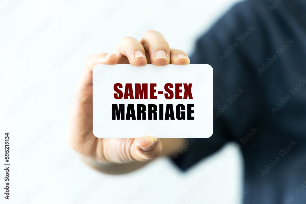 Same-sex marriage text on blank business card being held by a woman's hand with blurred background. Business concept about same-sex marriage. Same-sex marriage text on blank business card being held by a woman's hand with blurred background. Business concept about same-sex marriage.