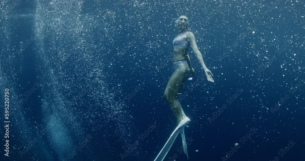 Freediver woman with fins glides underwater in ocean with air bubbles. Freediving water sport in tropical blue sea.