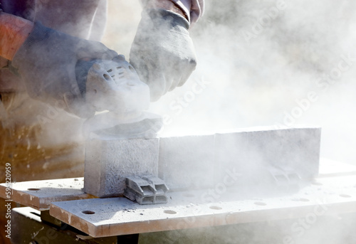 Photos A man cutting concrete balk with a lot of dust in the air