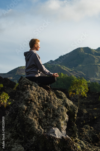 A young girl, sitting in a lotus position, arms to the sides, meditates in the mountains, in the first rays of the sun in the morning.