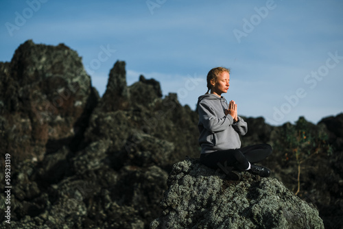 A young beautiful girl  a yogini  sits in the mountains  with her eyes closed  clasped her hands in namaste and meditates.