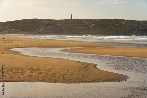 Frouxeira lighthouse since Valdoviño beach with its sand dunes in the coast of Galicia at sunset in a sunny day. A Coruña, Spain.