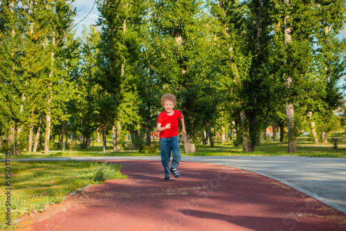 A curly-haired boy in a red T-shirt runs in the park on a treadmill. Children's charger.