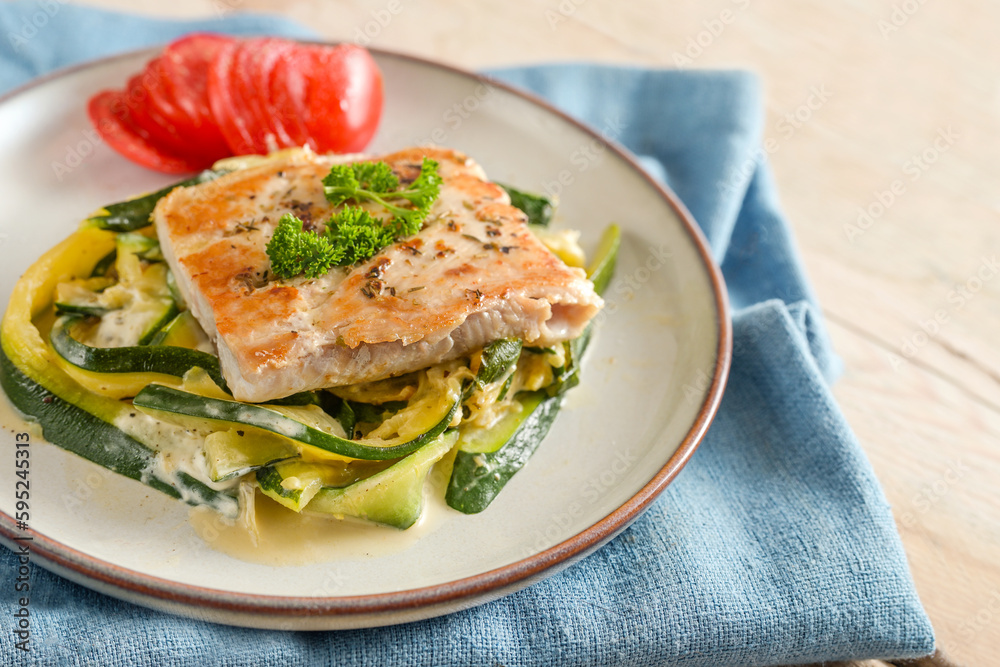 Salmon fillet with parsley garnish, zucchini vegetables and tomato on a light plate, blue napkin and a rustic wooden table, healthy low carb meal, copy space, selected focus, narrow depth of field