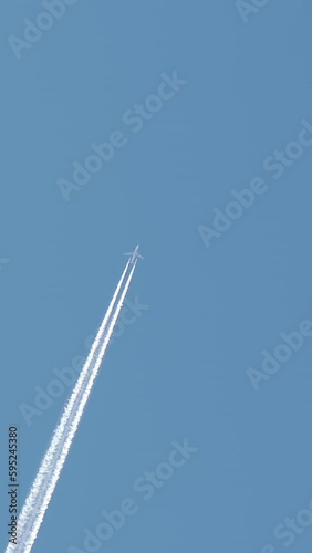 Jet aircraft plane with a bright white contrail as it flies across a blue sky. Vertical video photo