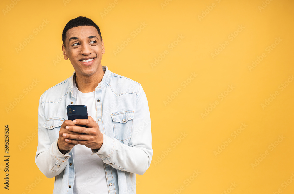 Smiling african american young man holding phone isolated on yellow studio background with copy space aside, african guy using mobile applications, texting. Smiling african american young man holding phone isolated on yellow studio background with copy space aside, african guy using mobile applications, texting.