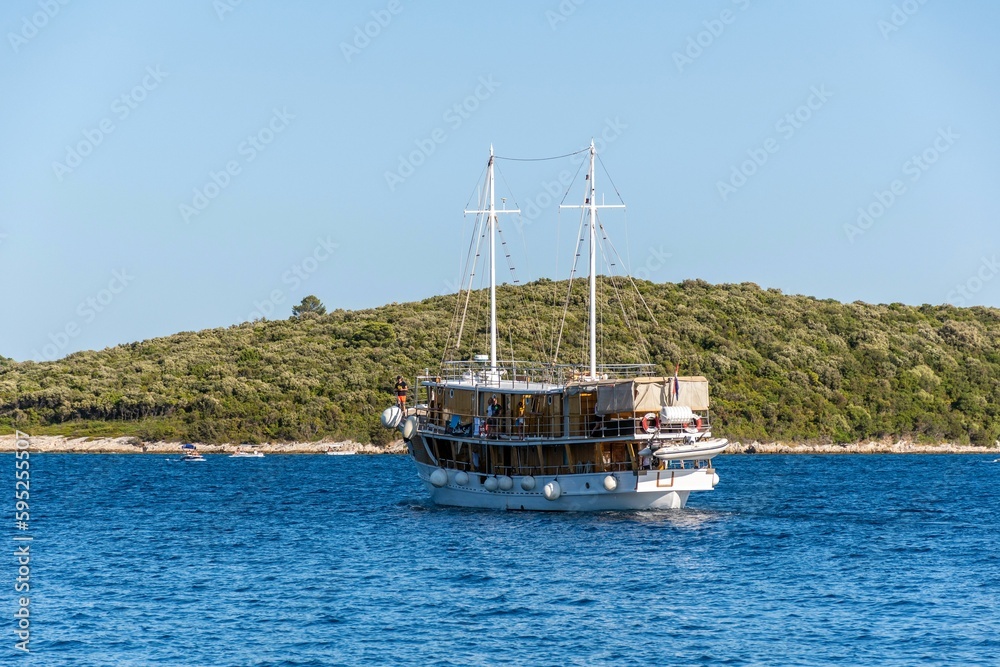 Sailboat drifts across the blue sea with a green hill in the background. Sailboat drifts across the blue sea with a green hill in the background.