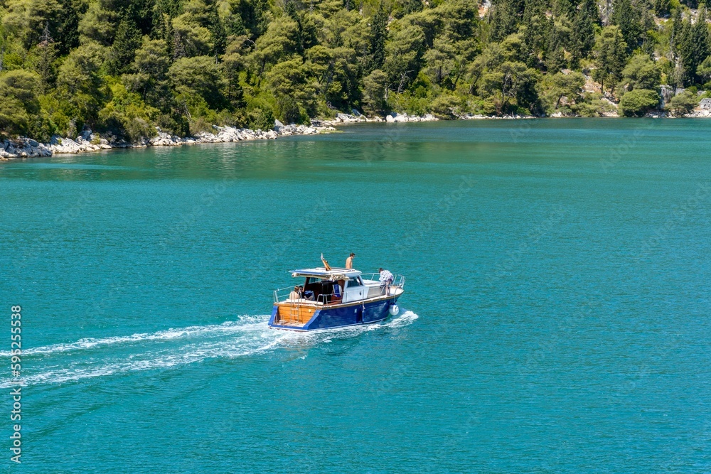 Boat traversing a tranquil blue body of water, with a picturesque backdrop of trees in the distance.