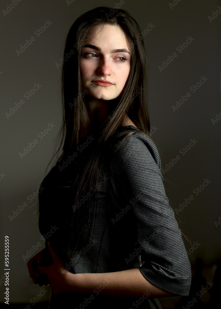 Beautiful girl in stylish clothes. Black dress, studio shot. The model poses in front of the camera. A student in a photo studio. Young beautiful girl
