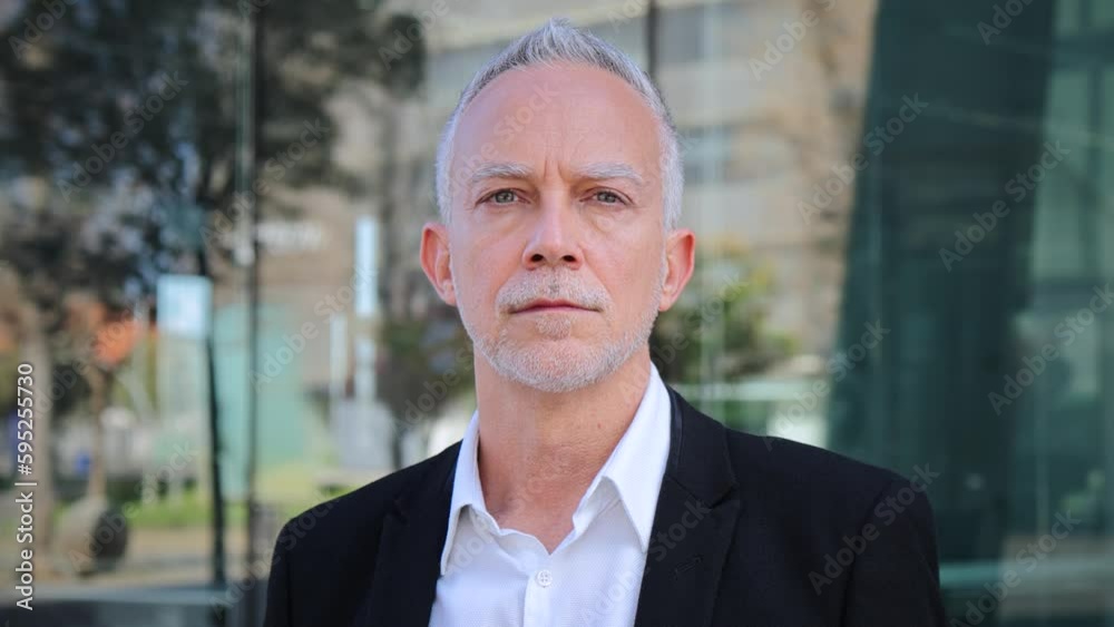 Close up portrait of a mature serious business man with aexecutive suit, gray hair, and successful attitude looking pensive at camera. Confident male welldressed corporate worker standing at workplace Close up portrait of a mature serious business man with aexecutive suit, gray hair, and successful attitude looking pensive at camera. Confident male welldressed corporate worker standing at workplace