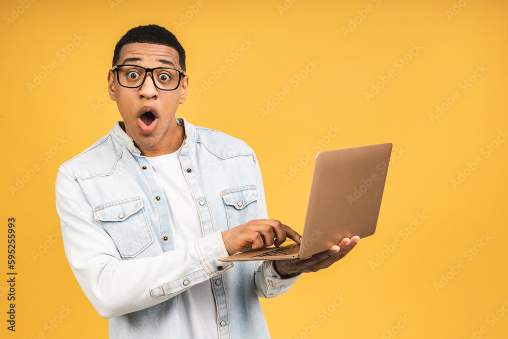 Smiling shocked amazed surprised african american businessman using laptop computer isolated over yellow background. Looking at camera. Smiling shocked amazed surprised african american businessman using laptop computer isolated over yellow background. Looking at camera.