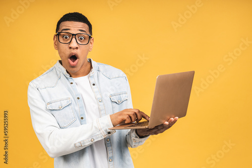Smiling shocked amazed surprised african american businessman using laptop computer isolated over yellow background. Looking at camera.