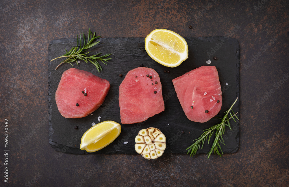 Seafood. Raw juicy tuna steaks  with spices and rosemary on a stone table. View from above.