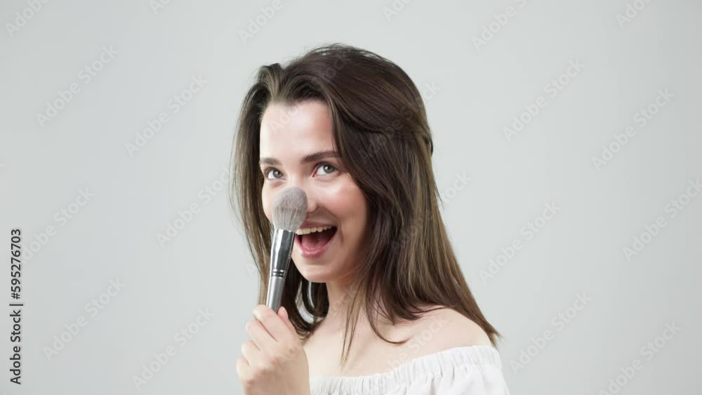 Beauty, face and makeup brushes for a female portrait on a light background for cosmetics. Aesthetic human model smiling and excited with self care tools, skin care and facial gloss for spa mockup
