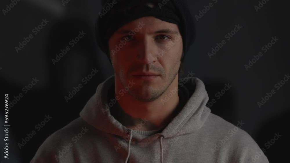 Portrait of man wearing black mask and looking in camera. Angry guy in hoodie and military balaclava standing in light of burning fire, screaming people in background